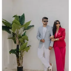 A chic and modern couple portrait against a clean white wall. The contrast between his light suit and her vibrant pink pantsuit creates a stylish and contemporary look.