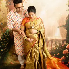 An intimate couple's portrait where the partner gently holds the baby bump. The rich gold of the saree glows under the studio lights.