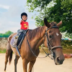A little rider gives a thumbs-up. We love seeing our kids feel proud and happy during their lessons.