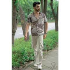 A full-length outdoor shot showcasing a casual, contemporary men's outfit. The natural, leafy background provides a great contrast to the stylish streetwear look.