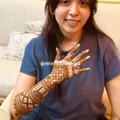 A happy bride showing off her minimal yet elegant back-of-hand design. Her relaxed smile and casual attire show that mehendi is a beautiful part of the entire wedding journey.