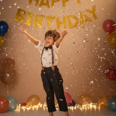 Capturing pure birthday joy as a young boy jumps mid-air, surrounded by falling golden confetti and a 'Happy Birthday' banner in the background.
