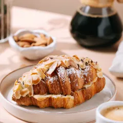 A close-up of the almond croissant, highlighting the flaky layers and almond topping. This detailed shot is designed to make the viewer's mouth water.