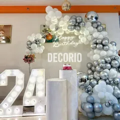 This clean and modern birthday decor uses a white and silver color scheme. The setup includes an elegant balloon arch, light-up '24' numbers, and pedestals for the cake, creating a sophisticated look.