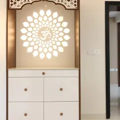 A close-up of another pooja unit featuring a beautiful backlit floral 'Om' motif. The intricate CNC-cut arch and white drawers provide a clean, traditional look with modern execution.