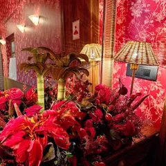 This entryway arrangement sets a dramatic tone with a profusion of red flowers against a bold, patterned wallpaper. The wicker lamp and miniature palm tree models add a touch of tropical, eclectic charm.