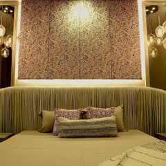 This bedroom showcases a custom-designed headboard that extends to the ceiling, featuring pleated fabric and a textured wallpaper panel. The hanging pendant lights on either side add a touch of modern luxury.
