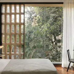 Soft morning light fills a daughter's bedroom in the Debris Block House. The large window offers verdant views, while the custom jaali screen provides ventilation and security, allowing the window to be left open.