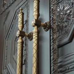 Our Raga Door Pull, with its neo-classical inspiration and intricate crisscross design, is pictured here against a masterfully carved wooden door. The Antique Brass finish enhances the handle's detailed texture, creating a harmonious dialogue between the two materials.