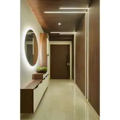 This long entryway is made to feel grand and elegant with our custom design. We used wood paneling on the ceiling and one wall, with integrated linear lighting, and added a sleek console with a backlit round mirror.