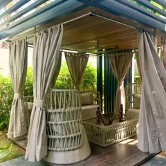 This angle showcases the elegant curtains and the high-quality woven furniture within the pergola. The structure provides a perfect frame for an intimate and stylish outdoor lounge.