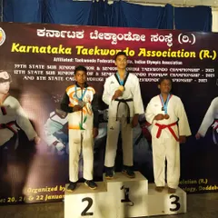 A student stands at the top of the podium, number one. This is from the Karnataka Taekwondo Association state championship. We aim for the gold.