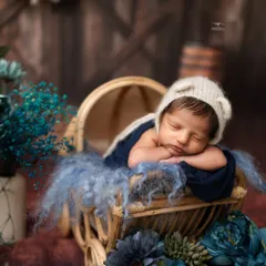 A classic newborn pose, with the baby resting his head on his hands in a rustic pram, surrounded by beautiful blue florals.