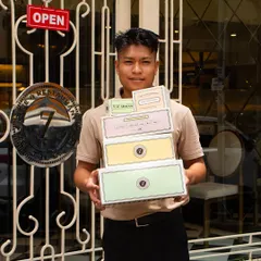 One of my team members proudly holding a stack of our signature boxes outside the café. We're ready to pack your favorites to go.