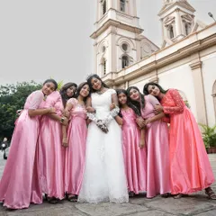 A fun and lovely photo of a bride surrounded by her bridesmaids in matching pink dresses, all sharing a happy moment outside the church on the wedding day.