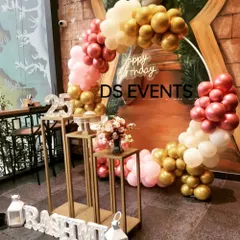This stylish setup for a 25th birthday features a circular backdrop with a rose gold, gold, and white balloon arrangement. The look is completed with a neon sign and modern gold-toned plinths for the cake.