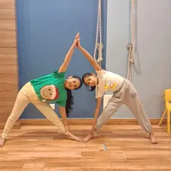Two girls work together in a partner yoga pose, demonstrating balance and teamwork. These activities help build trust and communication skills.