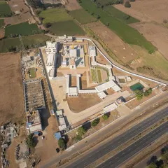 This top-down aerial view shows the complete layout of the Shiva Temple complex, located alongside the Hubli-Bengaluru highway. You can see the clear circulation paths, the Kalyani (temple tank), and the relationship between the built structures and open green spaces.