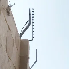 This is a real-world installation of a perimeter intrusion detection system (PIDS) on a stone wall. This system creates an electronic barrier that triggers an alarm if an intruder attempts to climb over.