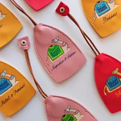 An array of colorful, hand painted leather keychains, each personalized for different families like 'Kapadia & Nahar' and 'Mittal & Poddar'. These make for wonderful, bespoke wedding or event favors.