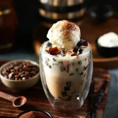 An indulgent coffee-based boba drink topped with a scoop of vanilla ice cream. The moody lighting and props like coffee beans and vanilla pods highlight the rich, aromatic flavors.