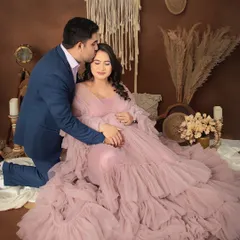 A sweet kiss on the forehead in our cozy boho setup. The couple shares a loving moment, with the mom-to-be seated and glowing in a dusty pink ruffled gown.