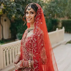 A smiling bride in her beautiful red wedding lehenga. I teach how to create makeup that not only looks good but also feels comfortable and lasts through all the emotions of the big day.