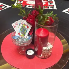 This centerpiece for our casino night is a perfect fusion of theme and elegance. We combined red roses, a pillar candle, and a glass filled with dice and playing cards, all arranged on a mirrored charger plate to amplify the glamour.