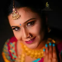 This studio portrait uses dramatic lighting to create a captivating look. The light from above highlights the intricate maang tikka and the model's expressive eyes, while the vibrant colors of her saree pop against the dark background.