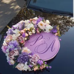 A personalized floral ring for a wedding car. This arrangement features the couple's initials on a lavender plaque, surrounded by a wreath of beautiful artificial flowers in matching shades.