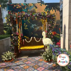 For a Mehendi ceremony with a traditional theme, I designed this stunning seating area. A classic wooden swing, or jhoola, is framed by a lush arch of fresh flowers and garlands. The centerpiece is a custom peacock crafted entirely from white flowers, set against a vibrant, artistic backdrop to create a picturesque spot for the bride.