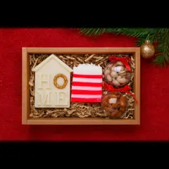 A cozy Christmas-themed gift box. This set includes a house-shaped soy wax candle, a striped candy cane soap, and two baubles filled with almonds and pistachios.