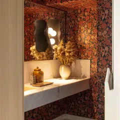 Inside the Bammi Residence powder room, a bold Sabyasachi wallpaper creates a luxurious and evocative backdrop. A sculptural wall sconce and a marble vanity complete the opulent look.