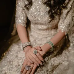 A close-up on the bride's hands, showcasing her sparkling rings and bracelets against her intricately sequined lehenga.