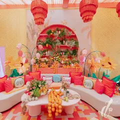 This vibrant seating lounge features a custom-built backdrop with tiered shelves of florals and fresh oranges. We used playful 'Oui' cushions and bold red and orange textiles on clean white sofas to create a fun, high-contrast look.