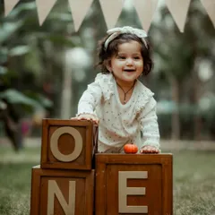 A beautiful, happy smile from a little girl celebrating her first birthday. The 'ONE' blocks and natural setting create a classic milestone portrait.