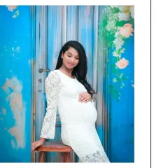 A relaxed and graceful seated portrait. The white lace dress and the bright blue backdrop create a striking contrast, resulting in a clean and contemporary maternity photo.
