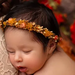 A close up on this sleeping baby's face, showing her soft cheeks and parted lips. The details of the autumn-toned floral crown add a beautiful touch.