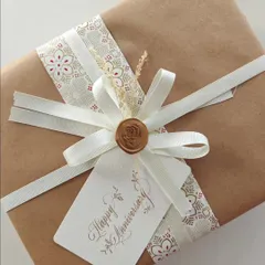 The final presentation of a personalized anniversary gift. The simple brown paper is elevated with decorative ribbon, a wax seal, and a handwritten "Happy Anniversary" tag.