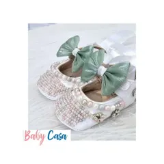 Step into comfort and style with these adorable, handcrafted baby shoes. These white bellies are adorned with pearls and a sweet green bow, perfect for a little princess.