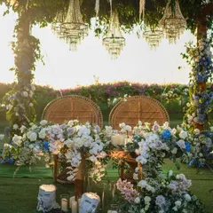 A romantic sweetheart table for an outdoor garden wedding, set under a canopy of hanging chandeliers and surrounded by lush blue and white flowers.