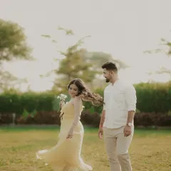 A playful moment during an outdoor pre-wedding shoot. The bride twirls with a flower in her hand, her hair catching the wind, as her partner looks on with a smile.