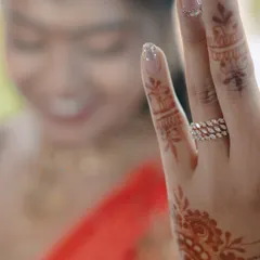 A detail shot focusing on the bride's engagement ring and the intricate mehndi on her hand, with her smiling face blurred in the background.