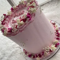 A tall and elegant pink cake decorated with a wreath of dried and preserved flowers. The different shades of pink and white create a soft, romantic look.