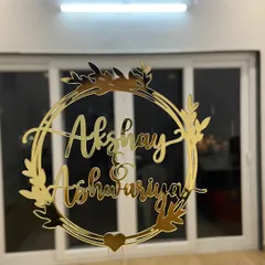 This elegant wreath design frames the names "Akshay & Ashwariya" beautifully. It's a timeless and romantic choice for any couple's special day, shown here in a brilliant gold mirror finish.