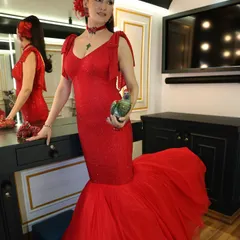 A full-length view of the stunning red mermaid gown. The dramatic tulle train and shoulder details were designed to make a powerful statement, perfectly capturing the client's 'boss babe' persona for her television appearance.