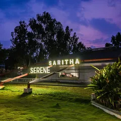 The marketing office for Saritha Serene, seen here at dusk. The illuminated signage and landscape lighting transform the building into a beacon, highlighting its unique architectural form against the evening sky.