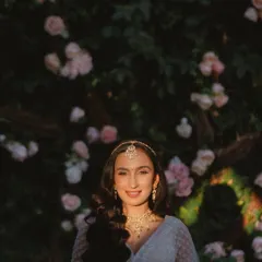 The bride's beautiful smile, illuminated by a perfect ray of sunlight against a wall of flowers. A moment of pure, natural radiance.