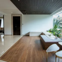 A serene lounge nook designed for quiet contemplation. The space is defined by a large picture window that opens up to a lush, green view, blurring the distinction between the built interior and the natural world outside.