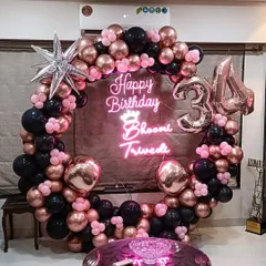 A glamorous 34th birthday setup right in the living room. We designed a full balloon ring with rose gold, black, and pink balloons, a personalized neon sign with the birthday girl's name, and foil number balloons.